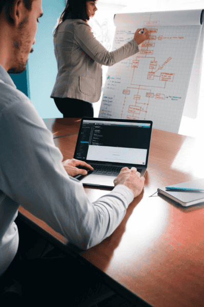 man with a laptop sat down and a lady standing drawing a graph on a board